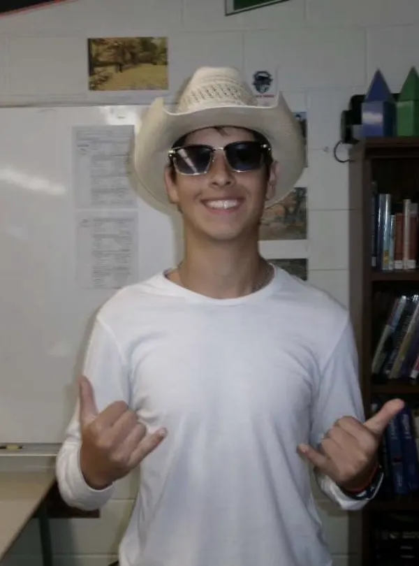 Ruben in a cowboy hat and sunglasses, smiling and throwing a shaka